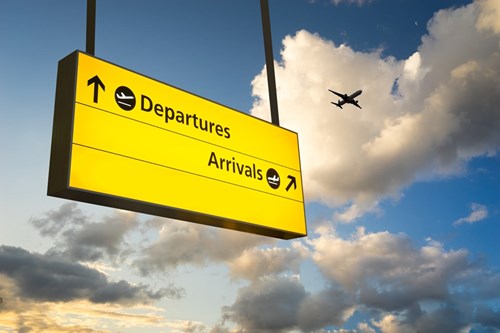 Yellow airport sign saying departures and arrives with a blue and white cloud sky and plane in background