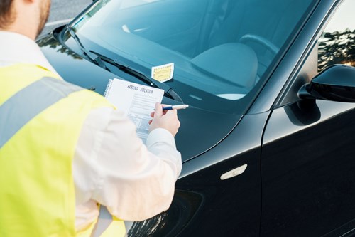 Enforcement officer in high-vis vest places parking ticket on windscreen