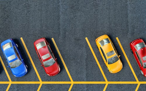 Aerial view of a parking lot with yellow lines marking bays and a yellow, blue and red car