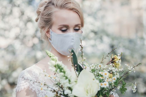 Bride wearing a face mask looks at her bouquet