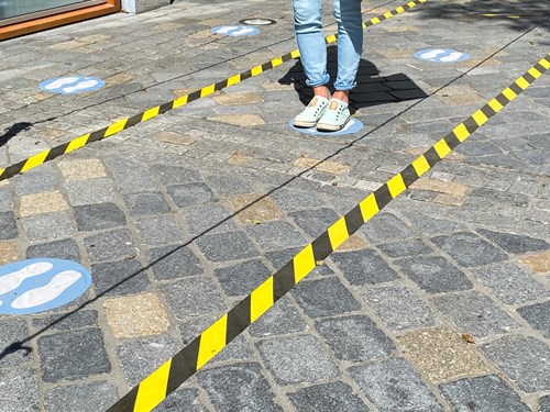 A woman in pale jeans and mint sneakers stands on a sticker of footprints between two rows of hazard tape