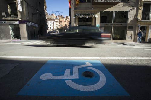 A parking space is painted with a blue block and wheelchair user icon, in the center of the space is a black sensor. Driving past on street is a car.