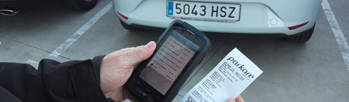 A man holds a smartphone and parking ticket up with a license plate in the background