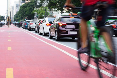 Red cycle lane with line of congested cars to the left.