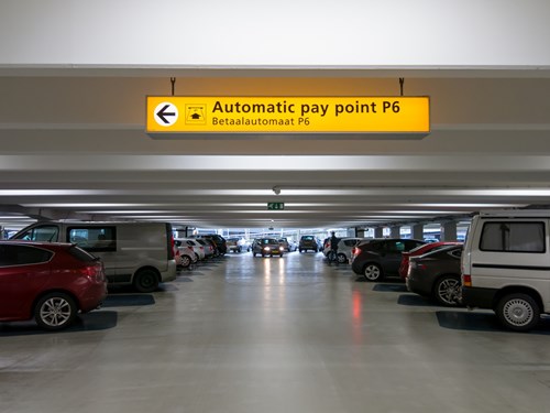 A yellow illuminated sign in a parking garage directing to a parking payment machine