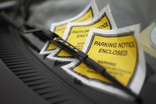 Three yellow parking tickets pinned beneath the windscreen wiper on a windscreen