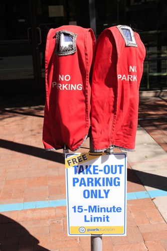2 parking meters covered in red bags and a sign displaying restaurant pick-up