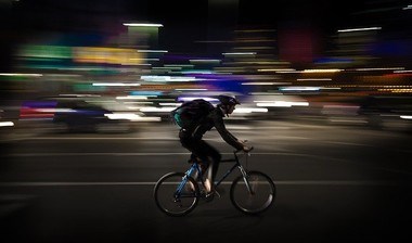 Delivery man on a cycles through a street at night