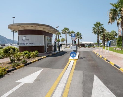 Entrance and exit lane of an outdoor parking lot with a kiosk to the left and palm trees and mountain views in the background