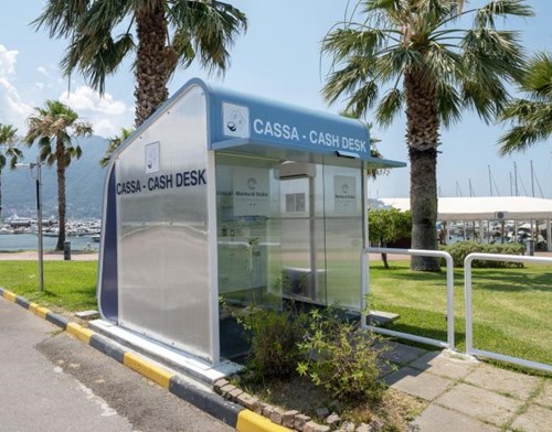 White and blue parking kiosk with yachts, mountains, ocean and palm trees in the background