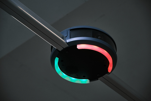 Circular, black parking guidance sensor attached to a ceiling displaying a red and green light