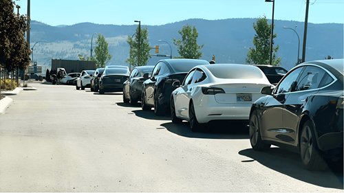 Queue of Teslas and EVs at the side of a road, waiting for an EV charger