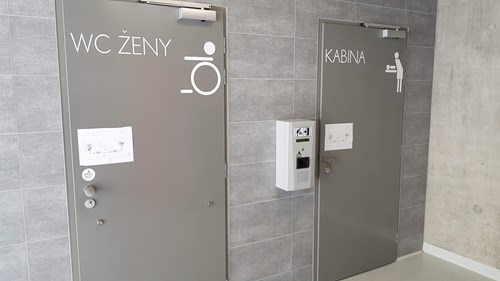 Grey tiled wall with two grey toilet doors, one displaying wheelchair user icon and the other a baby changing facility