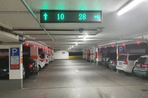 LED parking guidance signs fixed to a parking garage ceiling, displaying 10 spaces straight ahead and 28 spaces to the right.