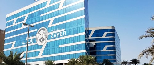 Glass office building with Arabic writing and man on the front, palm trees in foreground