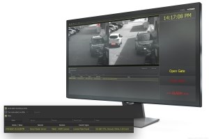 Computer monitor showing CCTV footage of a white car driving on road with cars parked on curb