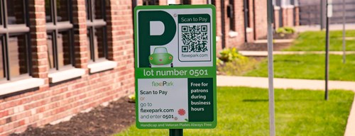 Green sign with P and QR code stands in a lawn with brick wall to the left