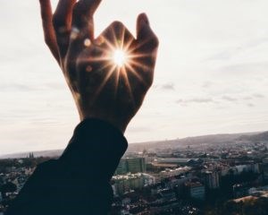 Man overlooking city holds hand up and sun shines through